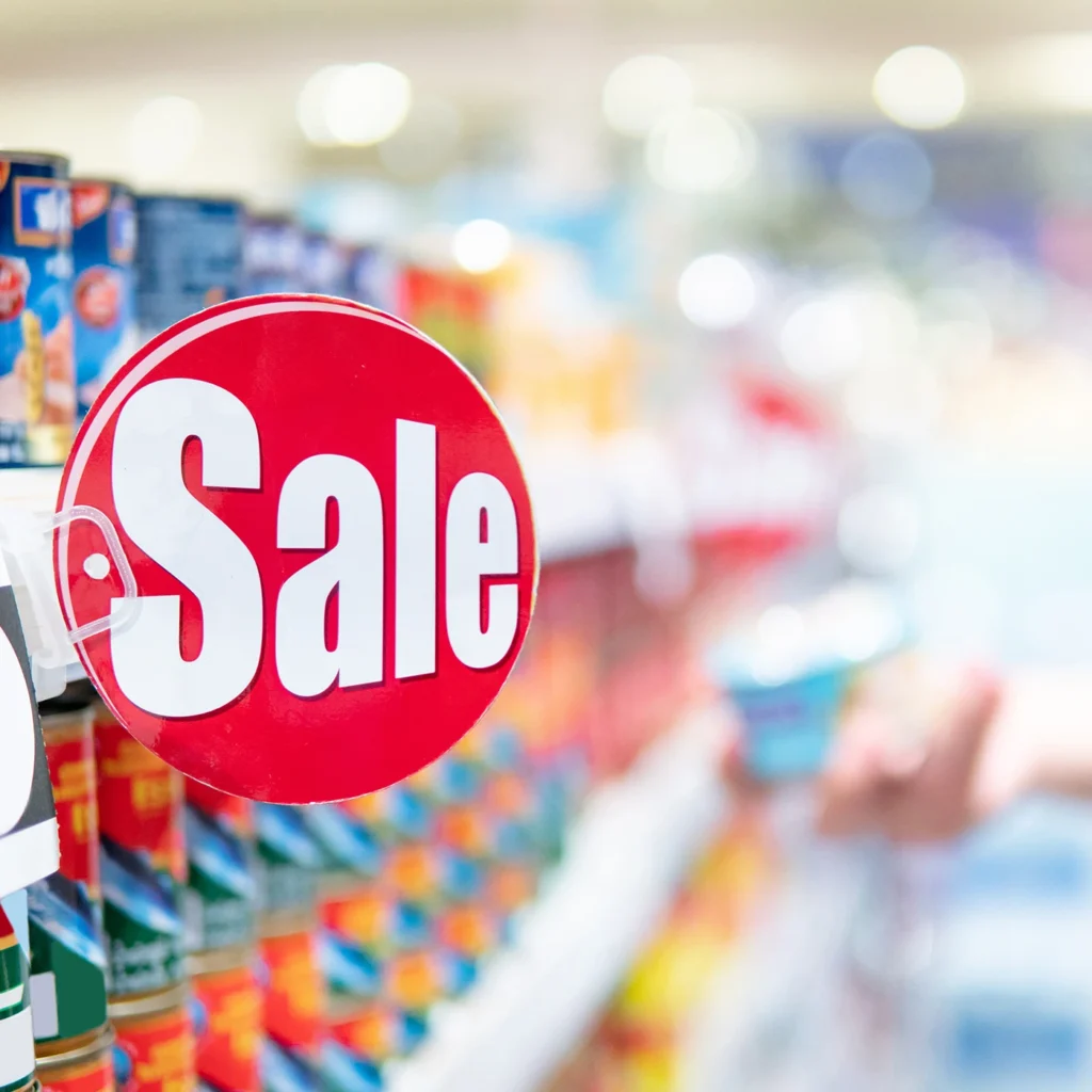 cliffedge marketing Red sale label on product shelf in supermarket with blurred male shopper choosing food package in the background.